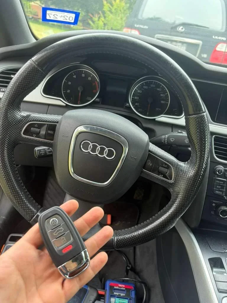 A car key held beside an Audi steering wheel